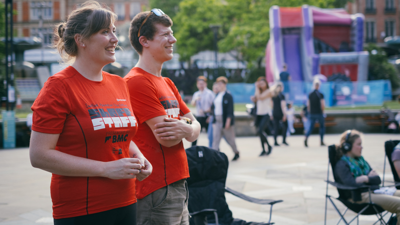 Two smiling ShAFF volunteers (Anna and Phil) are outside standing by audience members seated in deck chairs