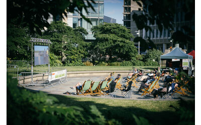 An outdoor cinema screen in Sheffield's Peace Gardens, rows of audience members are seated in deckchairs to watch the films