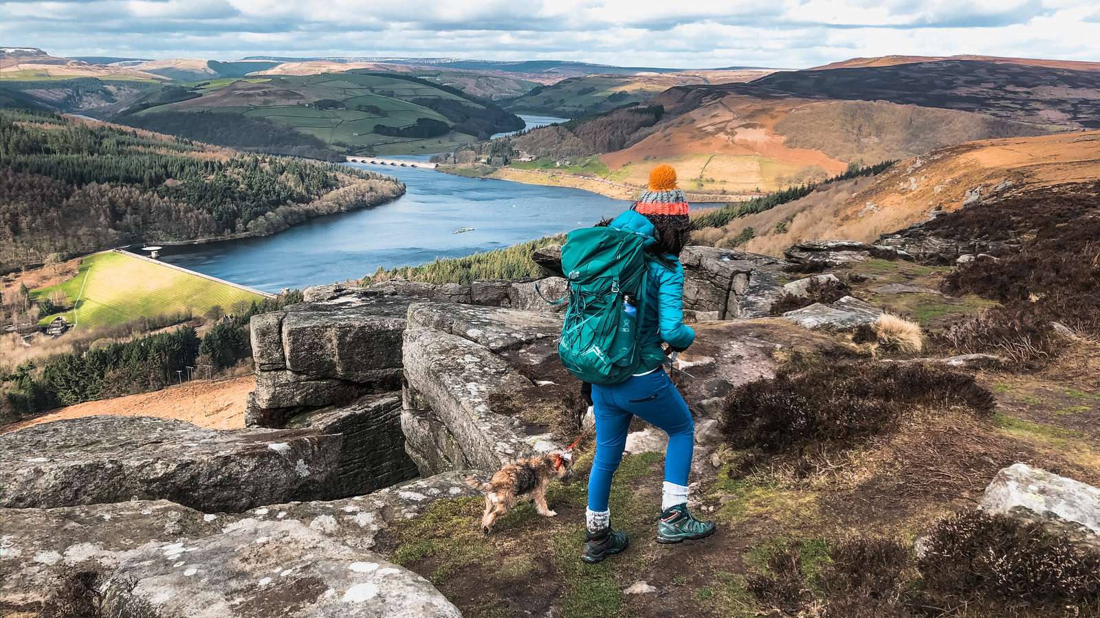 Hiker climbing a cliff edge overlooking a reservoir 