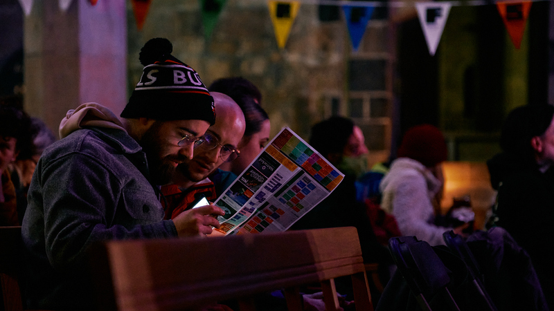 An audience member leans in to read the ShAFF programme in his hands, while waiting in a dimly lit cinema for the film to start