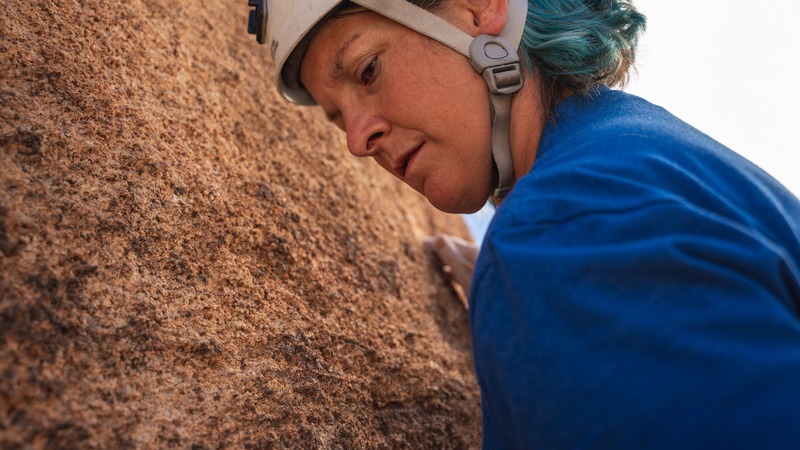 Poster image for the film Elevated. A climber wearing a white helmet leaning against a sandstone cliff.