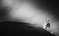 black and white image of a skier crossing skis in a trick, lit by a shaft of light in the darkness