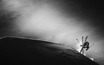 black and white image of a skier crossing skis in a trick, lit by a shaft of light in the darkness