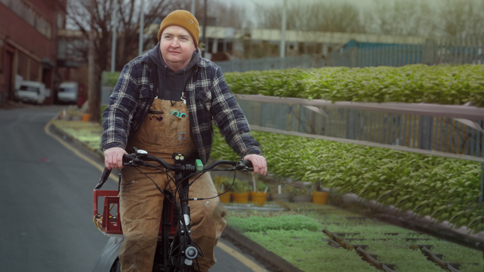 Farmer Luke Ellis rides his cargo bike along a city street lined by green plants