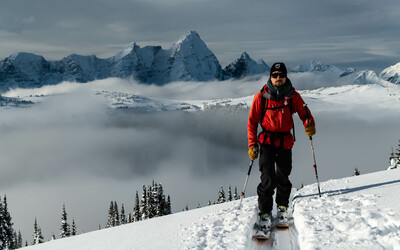 A skier skiing towards the camera above a coud inversion with jagged snowy peaks in the background.