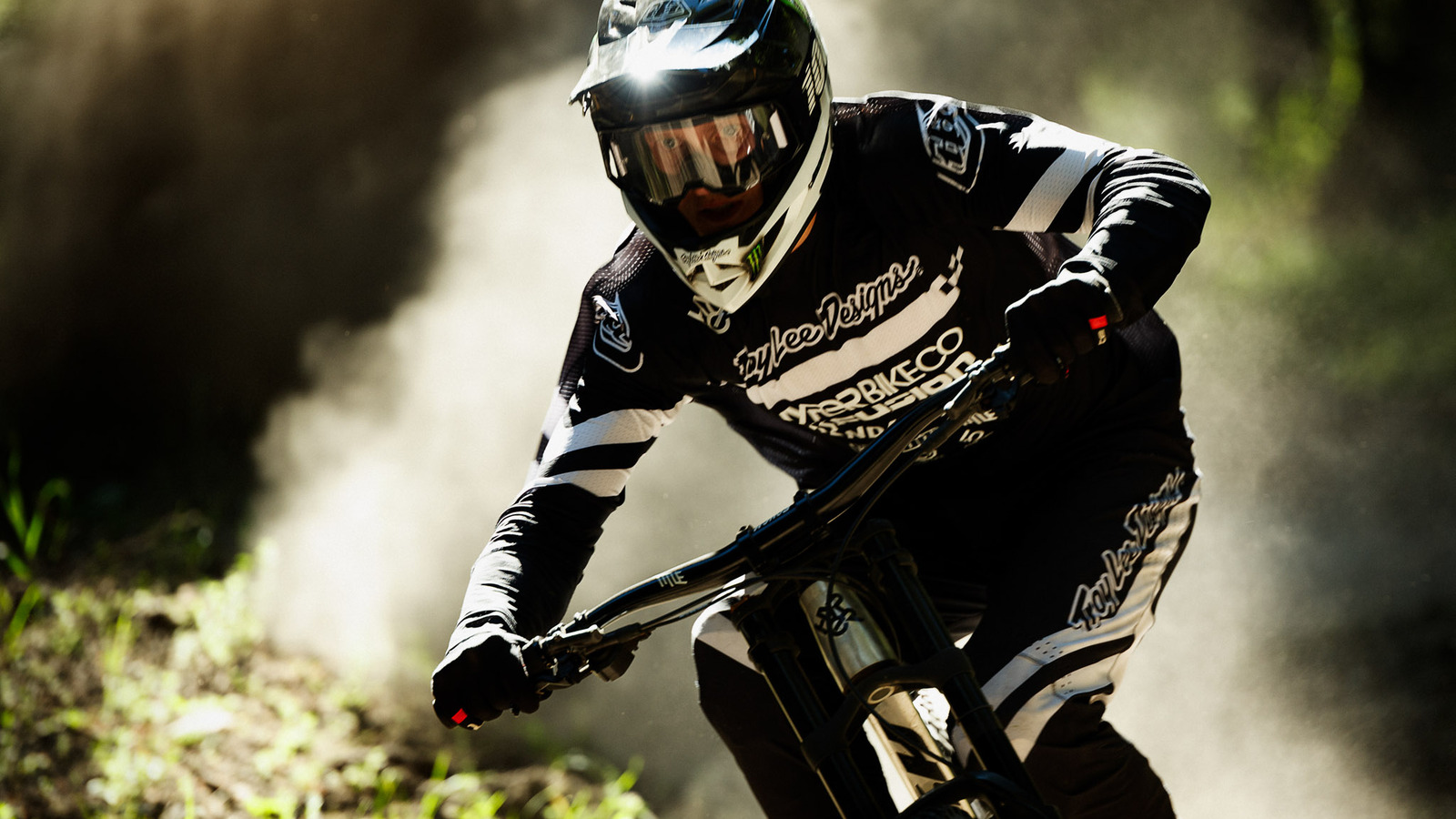 Action shot of a rider with a full-face hemet, plumes of dust shooting behind as they ride their bike towards the camera