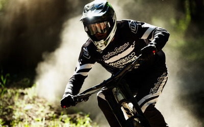 Action shot of a rider with a full-face hemet, plumes of dust shooting behind as they ride their bike towards the camera