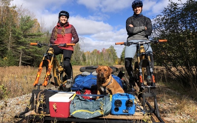Riding The Rails Poster image showig two cyclists and a dog on a home made contraption cycling along a disused railyway line