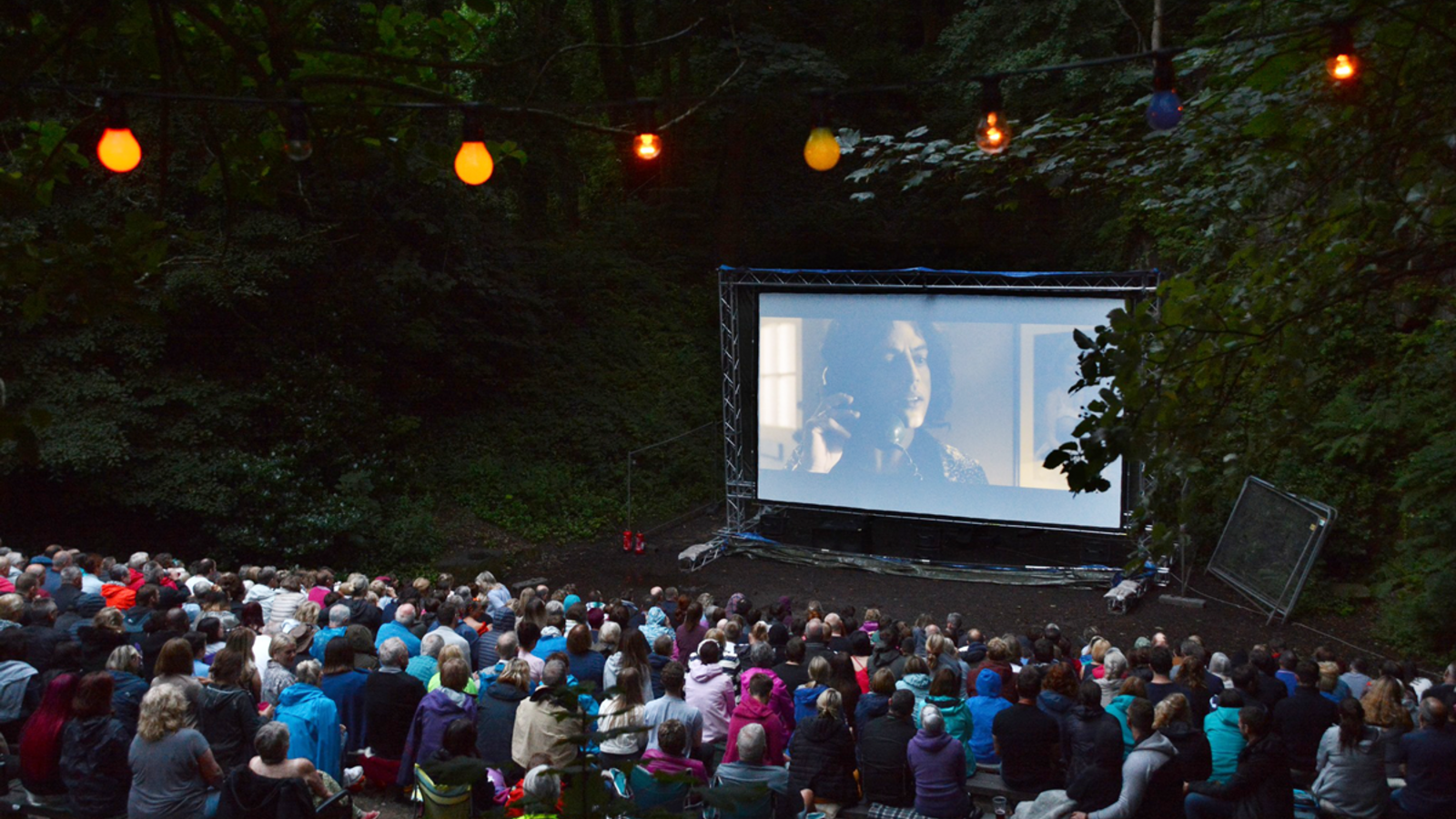 A group of people watching a film at an outdoor cinema surrounded by trees