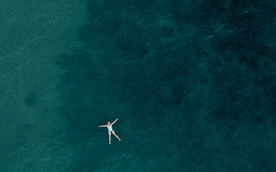 Poster image for the film Bluetits. Birds eye view of woman floating in the sea