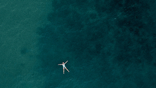 Poster image for the film Bluetits. Birds eye view of woman floating in the sea