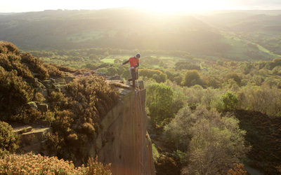 A climber stood at the top of a Gritstone edge looking down whilst belaying