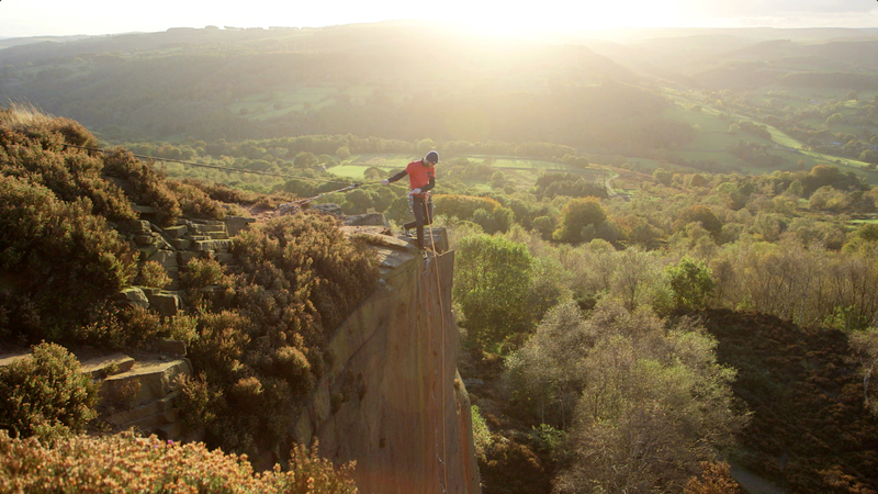 A climber stood at the top of a Gritstone edge looking down whilst belaying