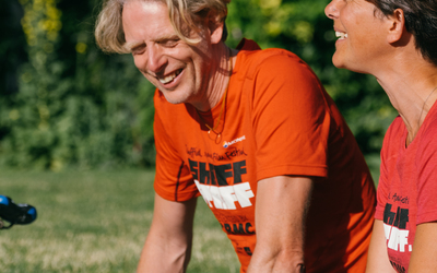 ShAFF director Matt Heason laughs in the sun while talking to a ShAFF volunteer, they are both wearing ShAFF Tshirts