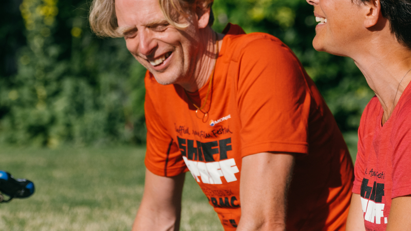 ShAFF director Matt Heason laughs in the sun while talking to a ShAFF volunteer, they are both wearing ShAFF Tshirts