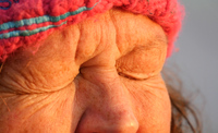 A lady wearing a fluffy winter hat scrunches her eyes up tight, close to the camera. It is sunrise and there is a golden light on her face.