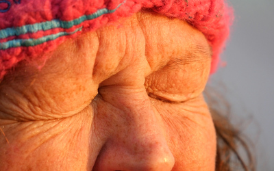 A lady wearing a fluffy winter hat scrunches her eyes up tight, close to the camera. It is sunrise and there is a golden light on her face.
