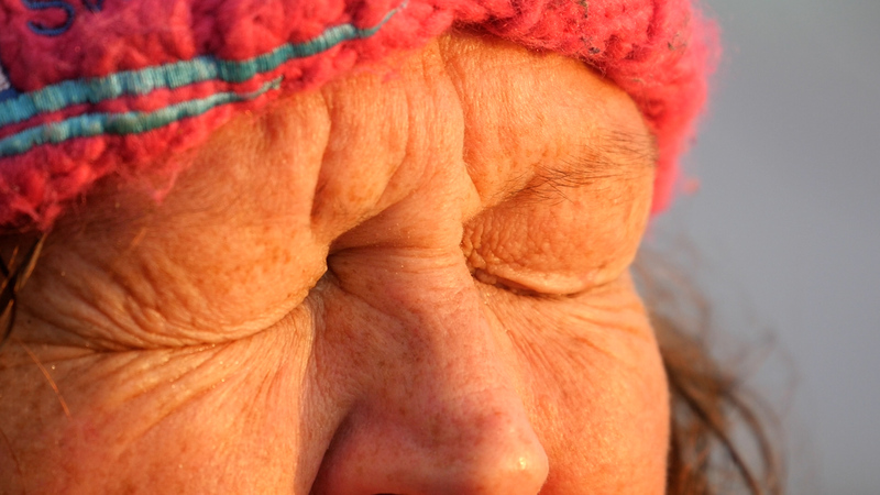 A lady wearing a fluffy winter hat scrunches her eyes up tight, close to the camera. It is sunrise and there is a golden light on her face.