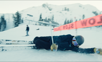 A skier sliding on their side under a SLOW sign.