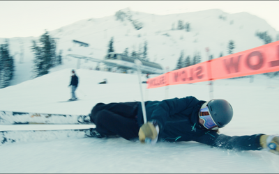 A skier sliding on their side under a SLOW sign.
