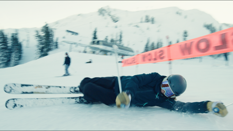 A skier sliding on their side under a SLOW sign.