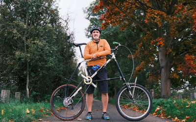 Jon stands behind his tall bike on a cycle path