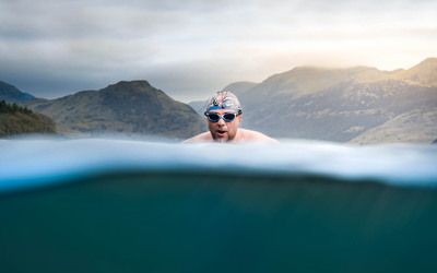 A white man swims in a lake with mountains behind