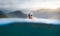 A white man swims in a lake with mountains behind