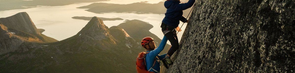 Freya, A 9 year old girl climbs a huge granite gliff ahead of her father, leo houlding. They are silhouetted by the low summer evening sun.
