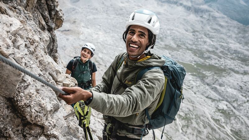 Climbers on granite rock going up a cable wearing Rab jackets and climbing gear