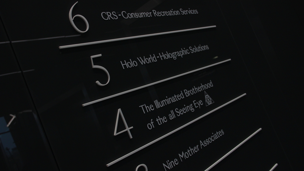 A lift sign showing office floor levels reads: 6 - CRS - Consumer Recreation Services; 5 - Holo World - Holographic Solutions; 4 - The Illuminated Brotherhood of the all Seeing Eye; 3 - Nine Mother Associates.