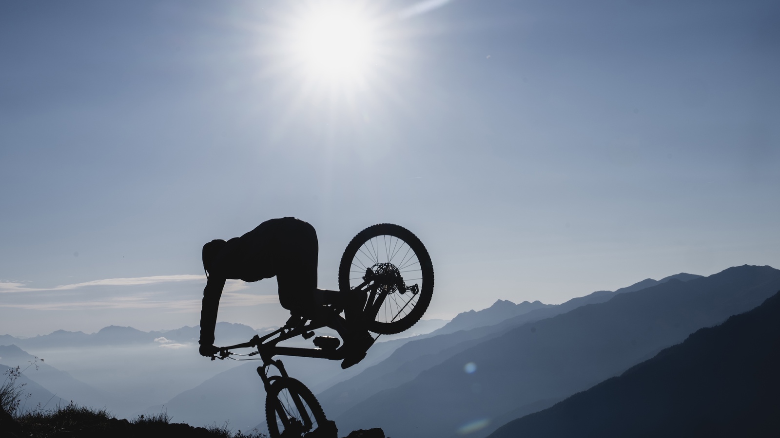 Young mountain bike athlete Bo Schwarz does a nose stall with his bike wheel up in the ground 1.5 meters off the ground. His body is silhouetted with the entire background cast in blue light.