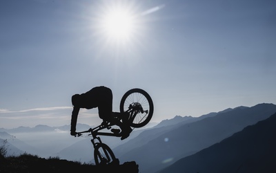 Young mountain bike athlete Bo Schwarz does a nose stall with his bike wheel up in the ground 1.5 meters off the ground. His body is silhouetted with the entire background cast in blue light.