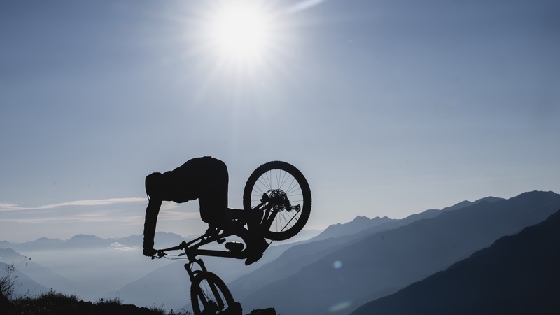 Young mountain bike athlete Bo Schwarz does a nose stall with his bike wheel up in the ground 1.5 meters off the ground. His body is silhouetted with the entire background cast in blue light.