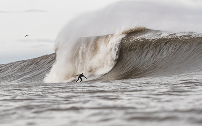 North Sea Surfer Sandy Kerr charges a huge wave wearing a natural rubber wetsuit