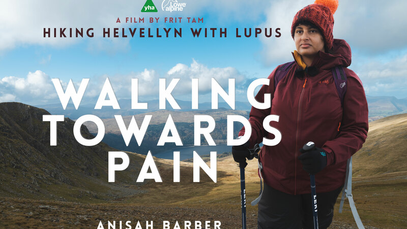 A young south asian woman dressed in a bobble hat, waterproof jacket and gloves, holds hiking poles and stares into the distance. The words "Walking Towards Pain" are large, alongside "Hiking Helvellyn with Lupus" and "Anisah Barber" - the main character in the film