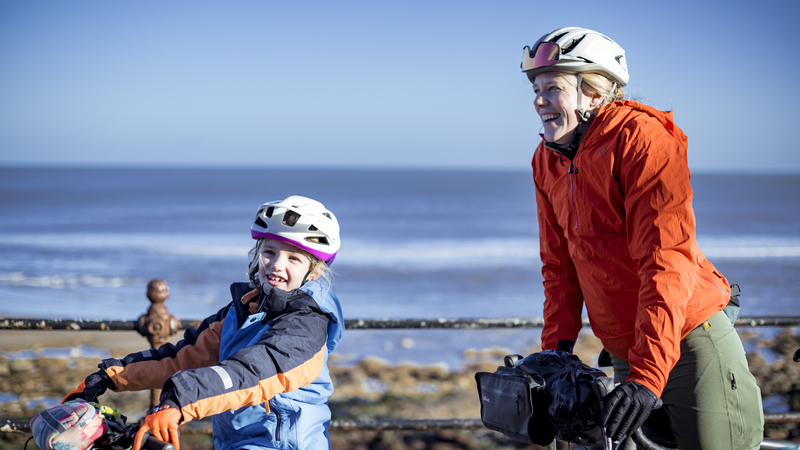 Cyclists, mother and young daughter, smiling with their bikes. 