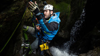 Canyoner Dale Strange reaching for anchor station above a dark gorge