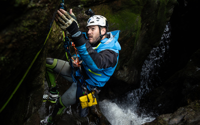Canyoner Dale Strange reaching for anchor station above a dark gorge