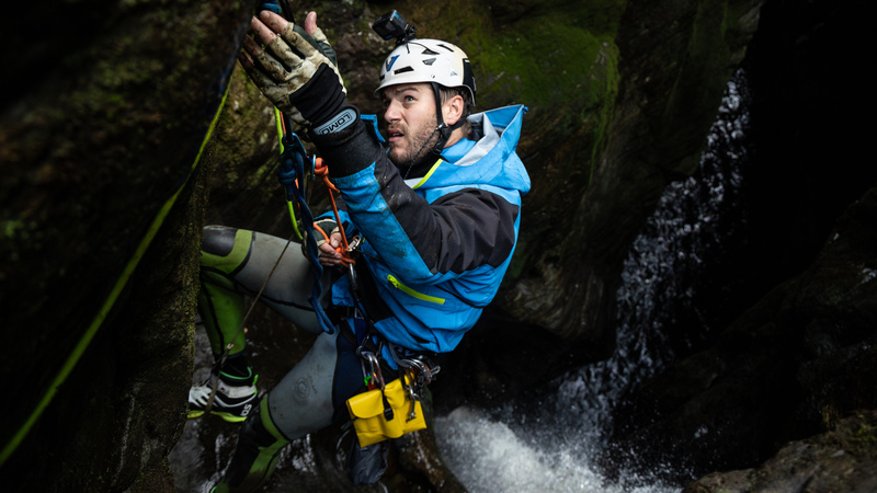 Canyoner Dale Strange reaching for anchor station above a dark gorge