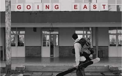 Filmposter, A skiers stands in front of a trainstation in Romania. The film title "Going East" is printed on the train station
