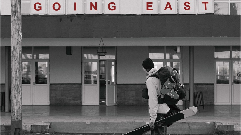 Filmposter, A skiers stands in front of a trainstation in Romania. The film title "Going East" is printed on the train station