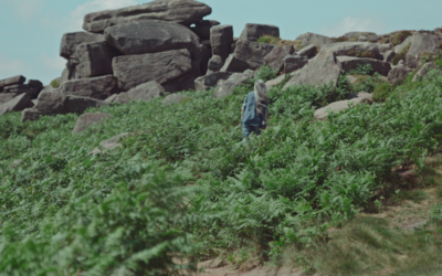 A still frame showing film protagonist Dal Kular climbing Stanage Edge, surrounded by rocks and foliage