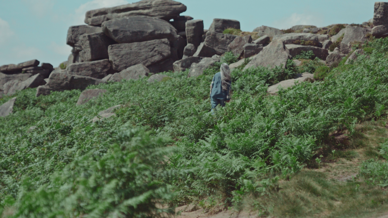 A still frame showing film protagonist Dal Kular climbing Stanage Edge, surrounded by rocks and foliage