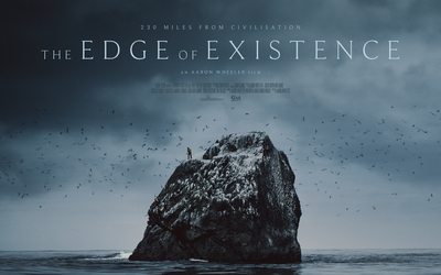 A man stands alone ontop of a small rock, surrounded by ocean.