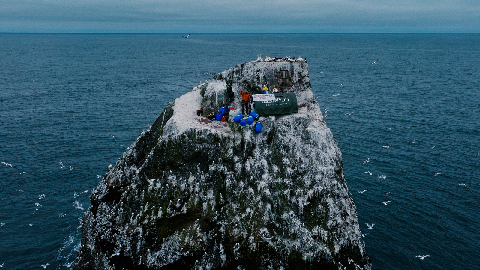 A man stands on a small cliff, surrounded by ocean.
