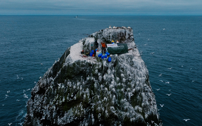 A man stands on a small cliff, surrounded by ocean.