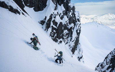 2 skiers climb a gully with skis and kit on their back