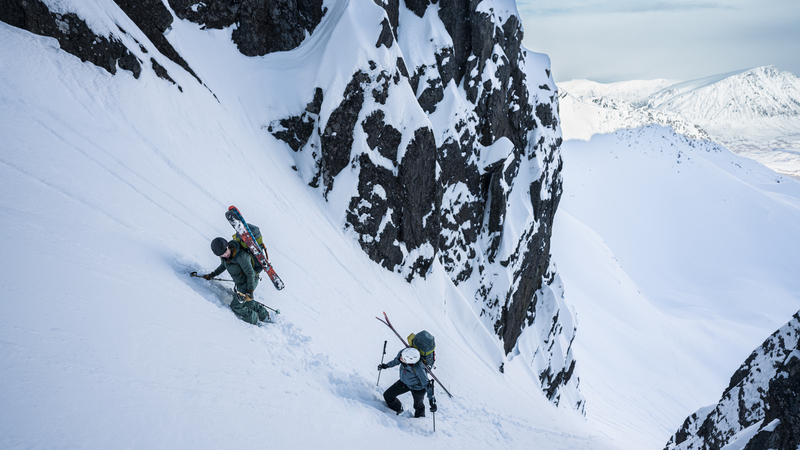 2 skiers climb a gully with skis and kit on their back