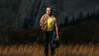 Geared up, professional climber Emily Harrington standing in front of a huge stone wall.
